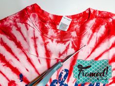 a tie - dyed shirt with scissors on it next to a pair of t - shirts