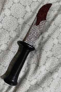 a black and white knife with some red beads on it's blade sitting on a bed sheet