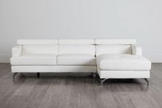 a white leather sectional sofa sitting on top of a hard wood floor next to a wall