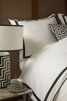 a bed with black and white pillows on top of it next to a night stand