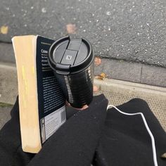 a person is holding a book and a coffee cup in their hand while sitting on the ground