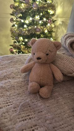 a brown teddy bear sitting on top of a bed next to a christmas tree