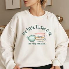 a woman sitting on top of a bed wearing a white sweatshirt with the words, feel fine things club it's very awesome