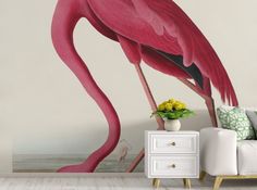 a pink flamingo standing next to a white couch in front of a wall mural