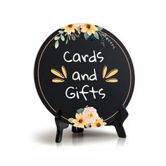 a black and white sign with flowers on it that says cards and gifts in gold lettering