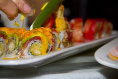 someone is cutting into some sushi rolls on a white plate with yellow and red toppings