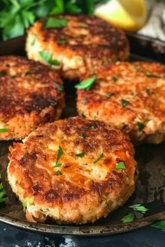 four crab cakes on a plate with lemons and parsley in the back ground