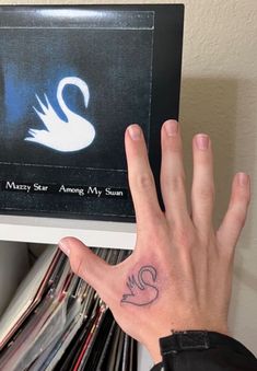 a person's hand with a swan tattoo on their left palm and an album in the background