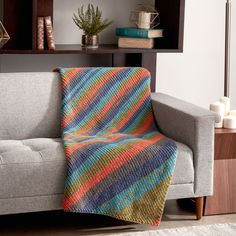 a couch with a blanket on top of it next to a book shelf and potted plant