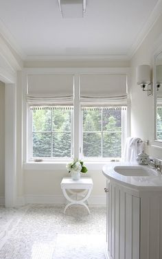 a white bathroom with two windows and a sink