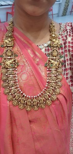 a woman wearing a pink saree with gold jewelry on her neck and necklace in the middle