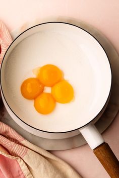 three eggs are in a white bowl on a pink surface next to a wooden spoon