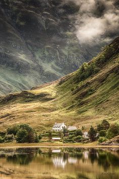 an image of a house in the middle of a mountain range with water and clouds