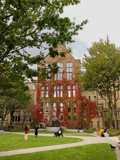 people are sitting on the grass in front of an old building with ivy growing all over it