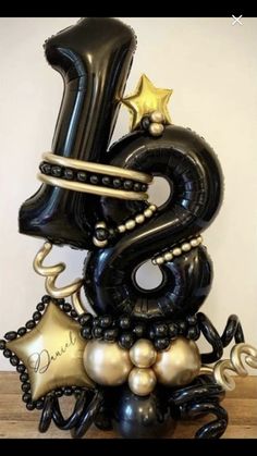 the number three balloon sculpture is decorated with black and gold balloons, stars, and confetti