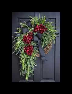 a wreath with red flowers and greenery hanging on a door