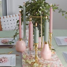 a table topped with pink and green candles next to a vase filled with greenery