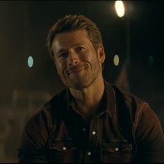 a man in a leather jacket is smiling at the camera while looking into the distance