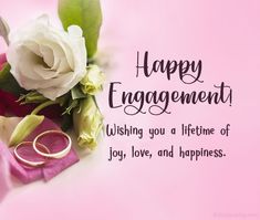 wedding rings and flowers on pink background with happy engagement message written in black writing,