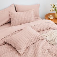 a bed with pink comforter and pillows on it next to a small wooden table