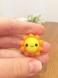 a hand holding a small yellow and orange sunflower brooch on top of a wooden table