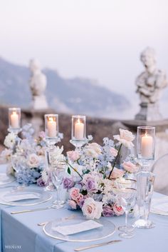 the table is set with white and pink flowers, candles and place settings on it