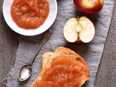 an apple and peanut butter spread next to two pieces of bread on a cloth with spoons