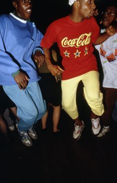 two young men are dancing together in front of people wearing blue and red shirts, one is holding a cell phone to his ear