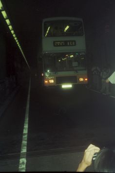 a double decker bus is coming down the street at night with people standing around it