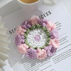 a crocheted flower sits next to a coffee cup on top of a paper