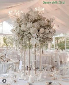 a tall vase filled with white flowers on top of a table covered in tables cloths