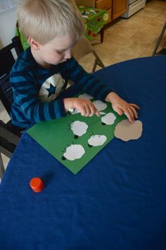 a young boy sitting at a table making a paper cutout with sheep on it