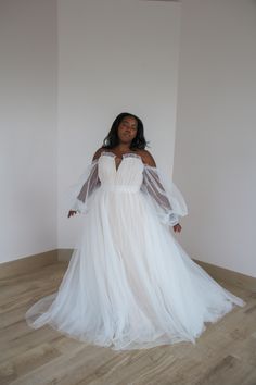 a woman in a white wedding dress standing on the floor with her arms out and hands behind her back