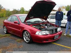 two men standing next to a red car with its hood open