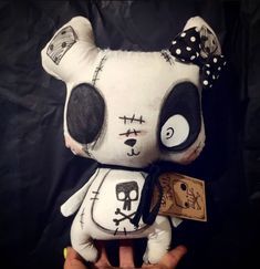 a hand holding a white stuffed animal with black eyes and a skull on it's face