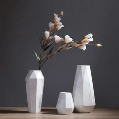 three white vases sitting on top of a wooden table next to each other with flowers in them