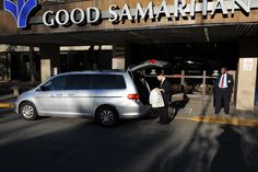 two men in suits are getting out of a silver minivan at the entrance to a hotel