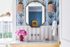 a bathroom with blue and white wallpaper, pink flowers in a vase on the sink