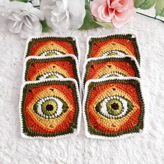 four crocheted coasters with an eye on them and flowers in the background