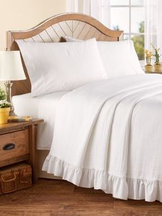 a bed with white sheets and pillows in a bedroom next to a wooden night stand