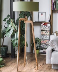 a wooden floor lamp with a green shade on it in a living room next to a couch