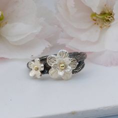 two silver rings with flowers on them sitting next to some pink flowers in the background