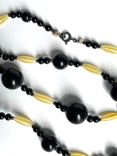 "Vintage Necklace Glass Beads Black and Yellow This lovely antique glass beaded necklace is made of big ball shaped jet black beads bookended with smaller round black beads in sets of two following by long oval yellow beads that has a milk satiny swirl. On very close inspection the largest black beads are graduated in size and almost look like a very dark purple but definitely read as black. There are some tiny metal spacer beads that appear to be textured, This necklace is strung on cord and closes with a spring ring clasp. I would guess. that this necklace is from the 1920s or 1930s and was made in Czechoslovakia. Measures approximately 25 1/2\" long. This is an authentic art deco necklace, a rare find and in good condition but show some loving wear from age and use. There are little fle Black Oval Beaded Necklaces, Black Necklace With Oval Spacer Beads, Vintage Black Handmade Beaded Necklaces, Vintage Black Large Beads, Vintage Large Black Beads, Black Vintage Large Beads, Vintage Black Jewelry With Wooden Beads, Vintage Black Necklace With Oval Beads, Vintage Black Beaded Necklace With Large Beads