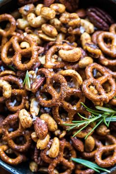 a bowl filled with pretzels, nuts and rosemary sprigs on top of a wooden table