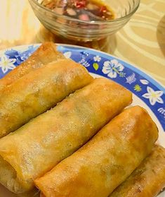 three spring rolls on a blue and white plate next to a bowl of dipping sauce