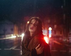 a woman standing in the rain at night with her arms around her neck and eyes closed