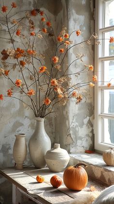 vases with flowers and pumpkins sit on a table in front of a window