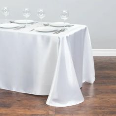 the table is set with white plates and silverware on it, along with empty wine glasses