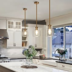 a kitchen with white cabinets and marble counter tops, two pendant lights over the island