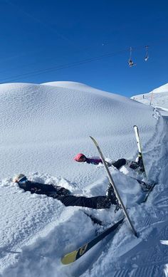 two skiers are laying in the snow with their skis propped up against them